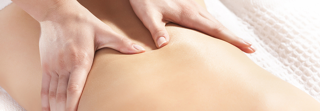 Eine Therapeutin massiert mit beiden Händen den nackten Rücken einer liegenden Frau.